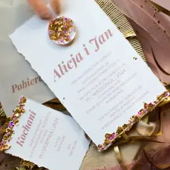 Eleganckie zaproszenia ślubne z piórami i złotymi zdobieniami.